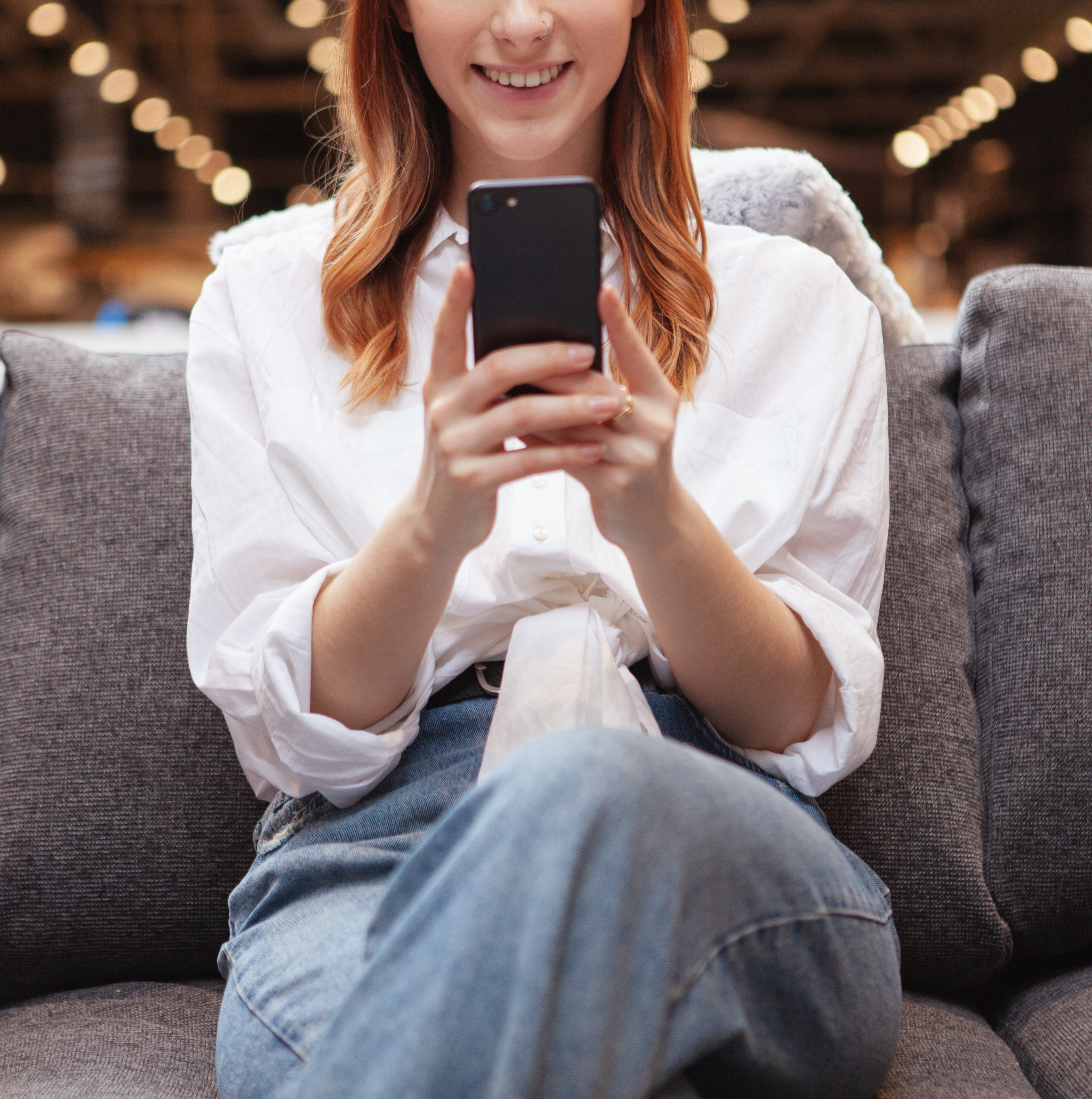 Cropped shot of a woman smiling, using smart phone while resting on a sofa